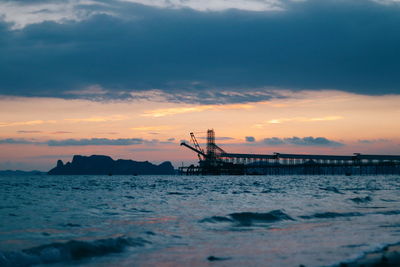 Silhouette crane in sea against sky during sunset