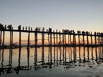 Silhouette people on bridge over sea against sky during sunset