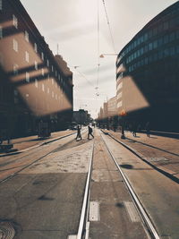 People walking on railroad tracks in city against sky