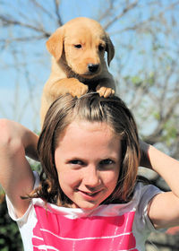 Close-up of smiling girl playing with puppy at park during sunny day