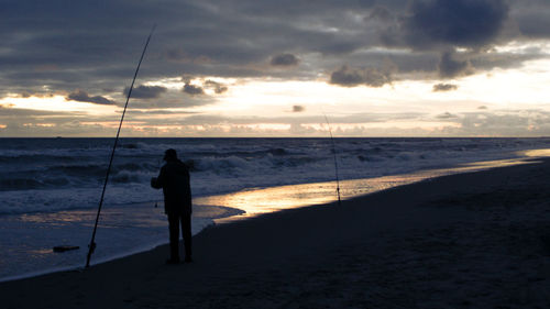 Silhouette man fishing at beach against sky during sunset