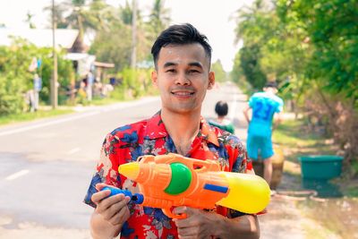 Portrait of young man holding water pistol standing on road