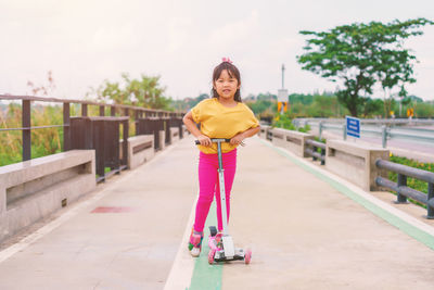 Little child girl to ride scooter in outdoor sports ground on sunny summer day.