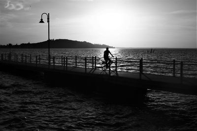 Silhouette man in sea against sky during sunset