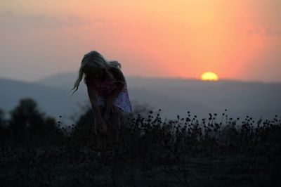 Girl bending on field against sky during sunset