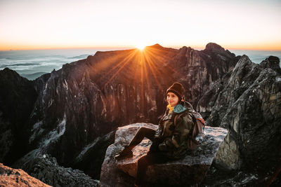 Woman sitting on mountain against sky during sunset