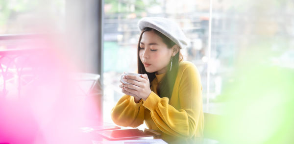 Young woman using phone while standing on window