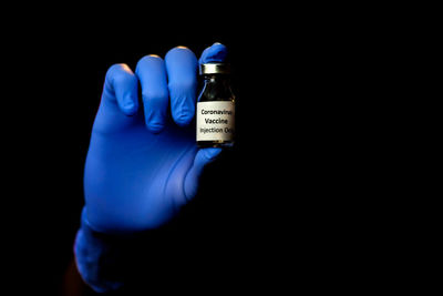 Close-up of hand holding bottle against black background