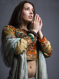 Beautiful woman in traditional clothing with hands clasped against gray background