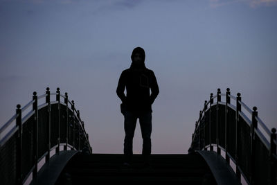 Silhouette man standing on footbridge against clear sky
