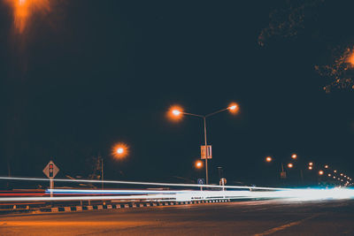 Illuminated light trails on road against sky at night