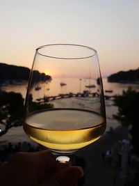 Close-up of hand holding wineglass against sky during sunset