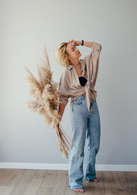 Full length of young woman photographing while standing against wall