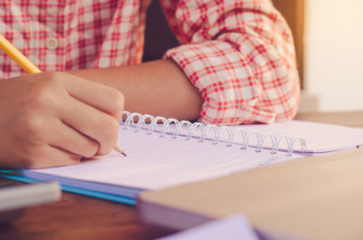 Midsection of man writing on book at table