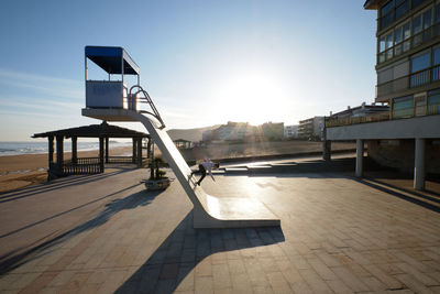 Side view of unrecognizable male skater riding down rescue tower located on seashore in summer