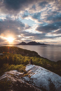 Man sitting on rock looking at mountain island at sunset