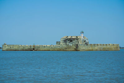 Old building by sea against clear blue sky