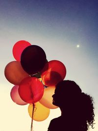 Silhouette young woman with colorful helium balloons against sky