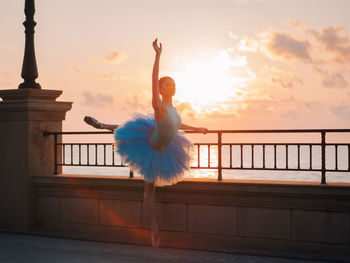 Woman ballet dancing by railing against sea