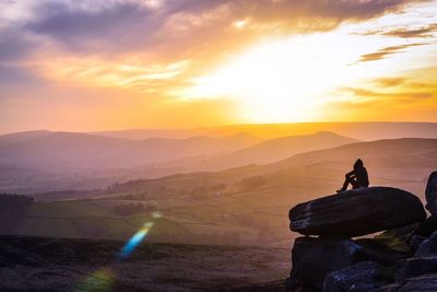 Rear view of man sitting on rock against mountains during sunset