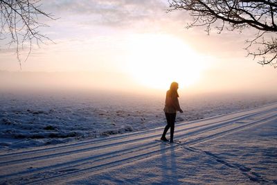 Full length of woman walking on snow covered landscape during sunset