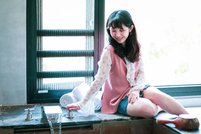 Portrait of smiling girl sitting on window at home