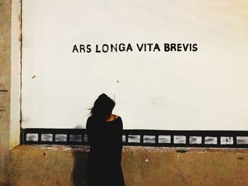 Woman standing by text on wall