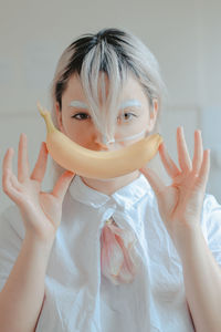 Close-up portrait of woman with painted face holding banana against white background
