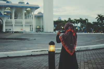 Rear view of woman photographing mosque with smart phone from footpath