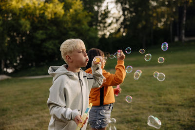 Boy blowing bubbles with female friend standing in playground at summer camp