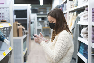 Woman wearing face mask and protective gloves in store uses phone. today people lifestyle concept