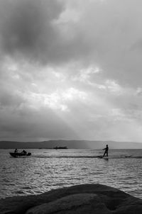 Silhouette man wakeboarding in sea against cloudy sky