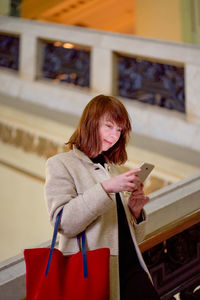 Woman using phone while standing by railing