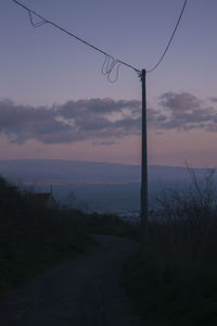 Silhouette electricity pylon by street against sky during sunset