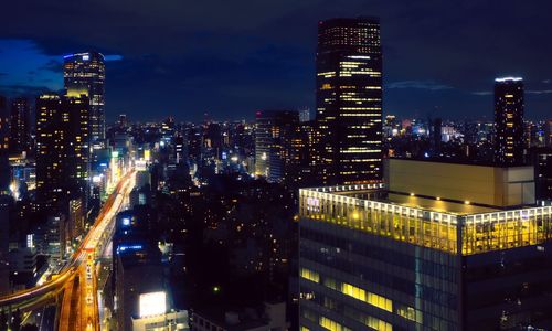 Illuminated modern buildings in city against sky at night