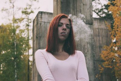 Portrait of beautiful young woman standing against trees