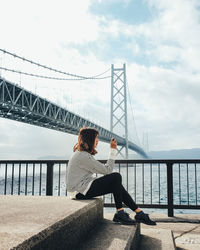 Full length of woman sitting by akashi strait bridge over sea