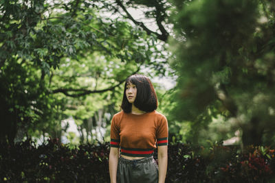 Thoughtful young woman looking away while standing against trees in park