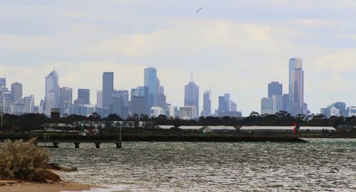 City at waterfront against cloudy sky