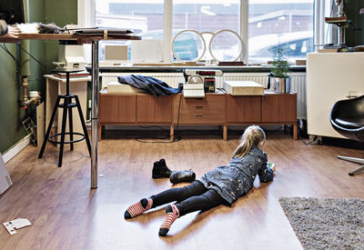 Rear view of girl lying on hardwood floor at eyeglasses workshop