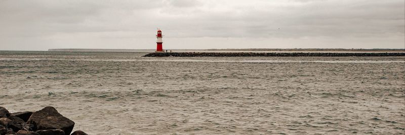 Lighthouse on beach by sea against sky