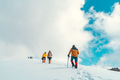 Full length of hikers walking on snow covered land against sky