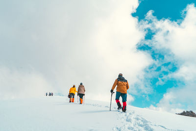 Rear view of people skiing on snowcapped mountain against sky