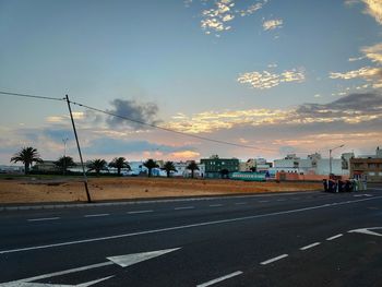 Road by city against sky during sunset