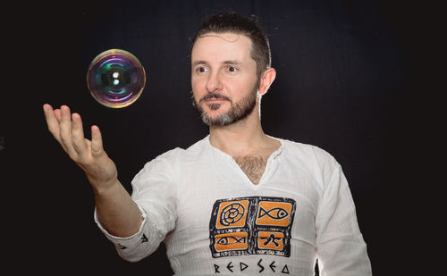 Portrait of man holding bubble against black background