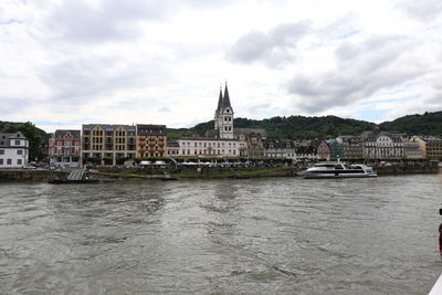 Buildings at waterfront against cloudy sky