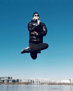 Fashionable man in mid-air over lake against sky in city