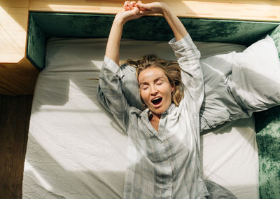 Portrait of beautiful young woman in pajamas lying in bed, stretching after waking up