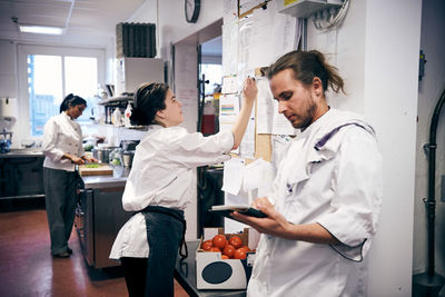 Female chef making checklist while colleagues working in kitchen