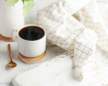 A white mug with black coffee, a branch with green leaves, an empty board